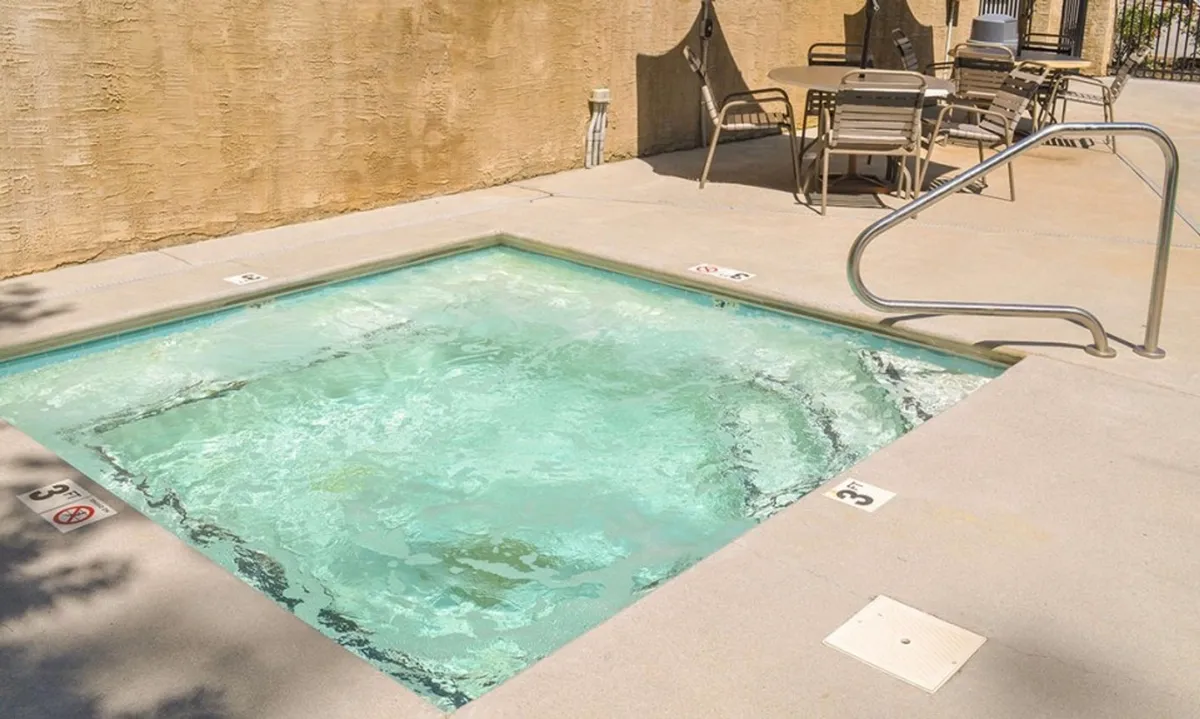 A sparkling spa pool surrounded by comfortable chairs and a poolside railing, set in a communal outdoor area. The scene evokes fun and togetherness, offering a place for families to socialize, unwind, and make memories after a day out.