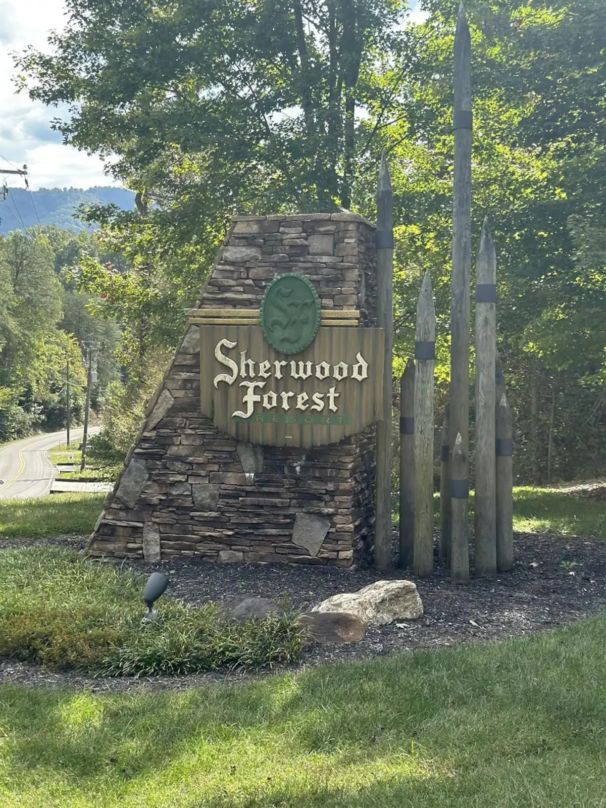 The Sherwood Forest sign marks the entrance to a welcoming cabin community, with a solid stone structure and rustic wooden poles set against a backdrop of lush greenery. The entrance hints at a sense of arrival and the excitement of exploring everything the neighborhood and its amenities have to offer.