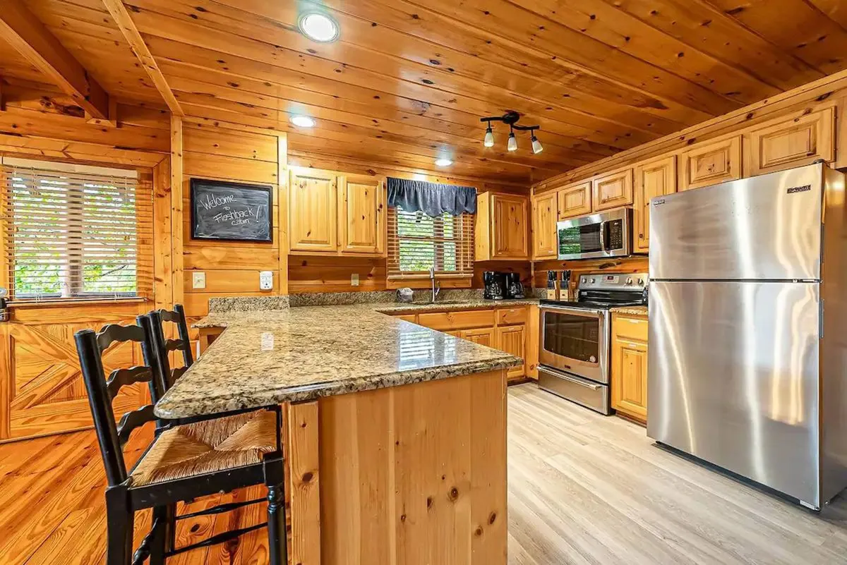 This image features a bright, updated kitchen with granite countertops, wooden cabinets, stainless steel appliances, and a welcoming chalkboard message. The open layout hints at a space perfect for cooking and gathering, with plenty of counter space and modern amenities front and center.