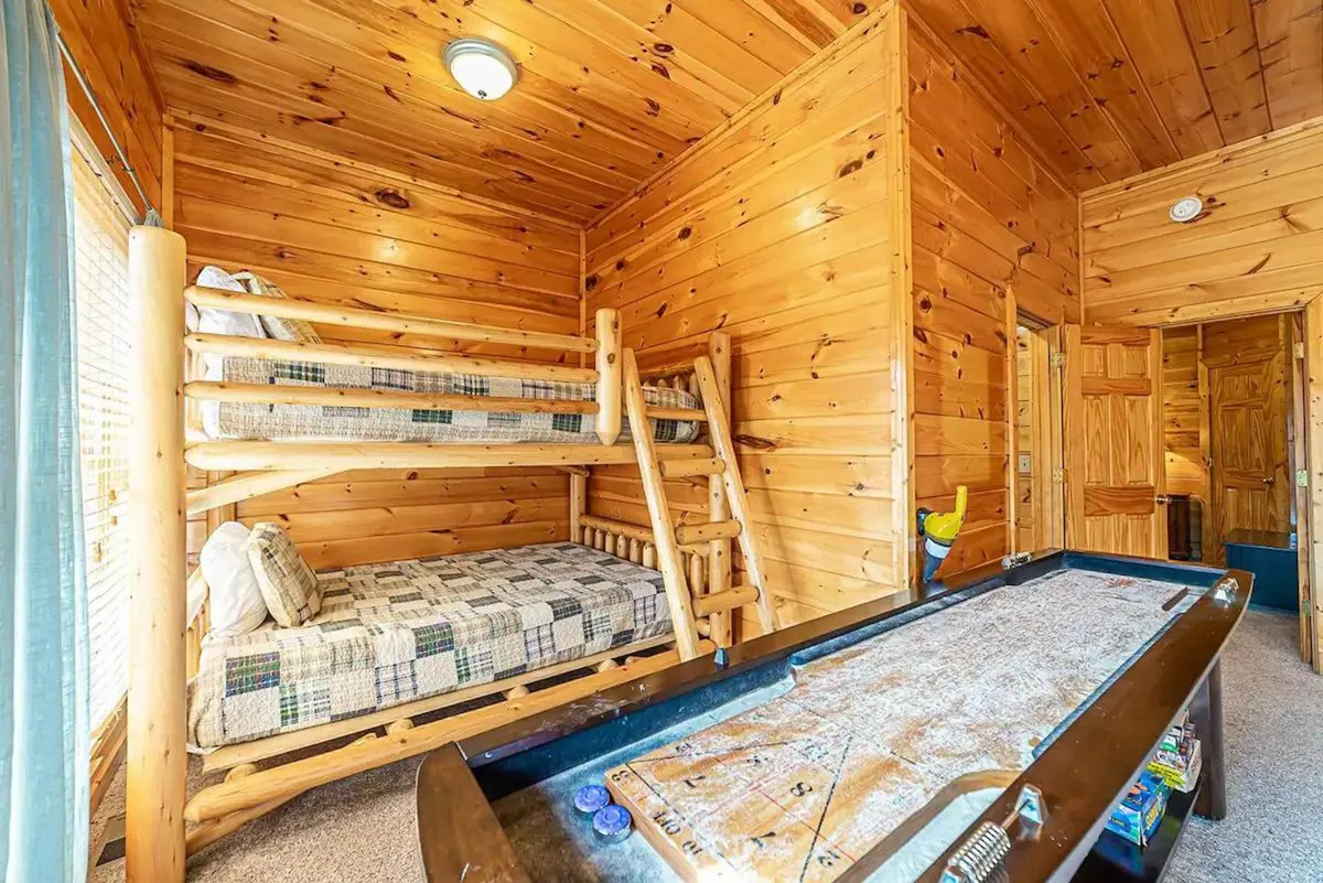 A playful bedroom featuring bunk beds against wood-paneled walls and an air hockey table, capturing a family-friendly atmosphere. Ideal for kids or guests seeking both rest and entertainment.